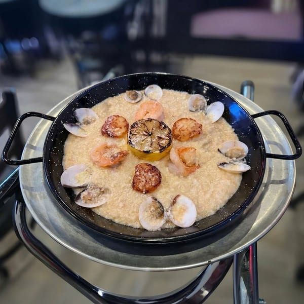 Seafood paella in a black pan with shrimp, clams, and a grilled lemon on a metal stand.