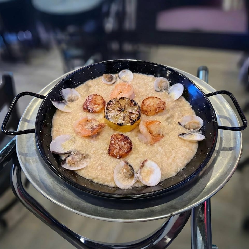 Seafood paella in a black pan with shrimp, clams, and a grilled lemon on a metal stand.