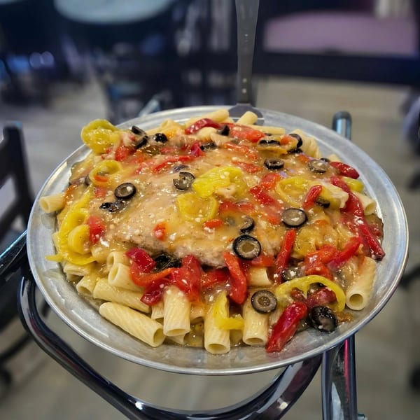 Chicken riggies with red and yellow peppers, black olives, and creamy sauce on a metal plate.