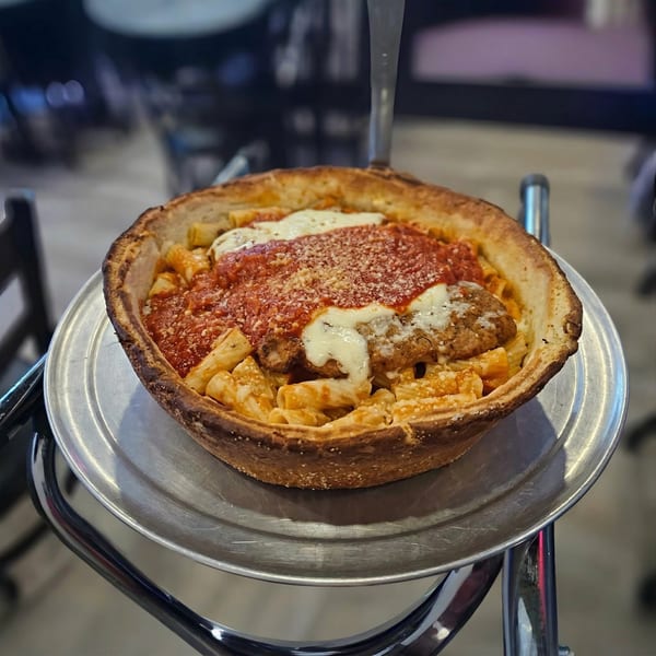 Deep dish pizza with pasta, chicken parmesan, marinara, and melted cheese on a metal stand.