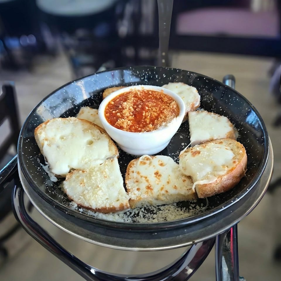 Cheesy garlic bread slices with a side of marinara sauce, served on a black skillet.