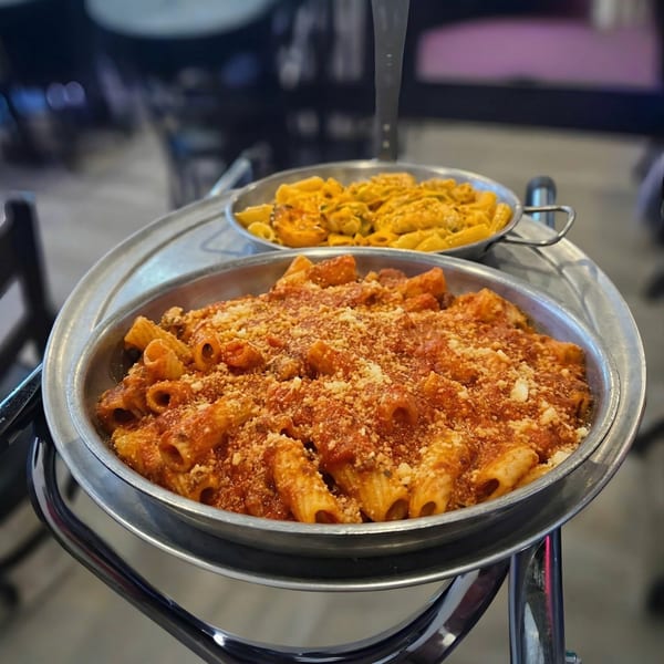Two metal pans of pasta, one with red sauce and parmesan, the other with creamy orange sauce.