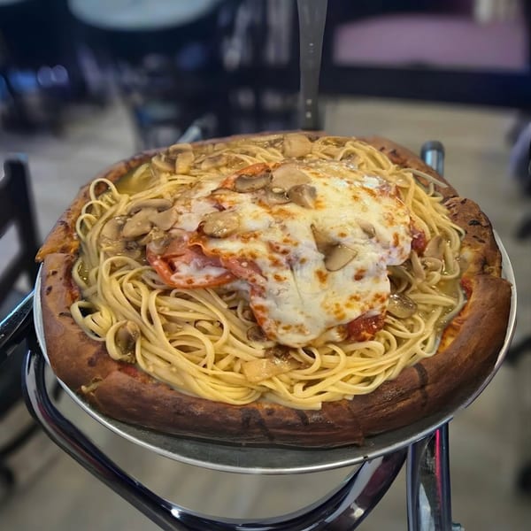 A pizza with a thick crust, topped with spaghetti, mushrooms, and melted cheese.